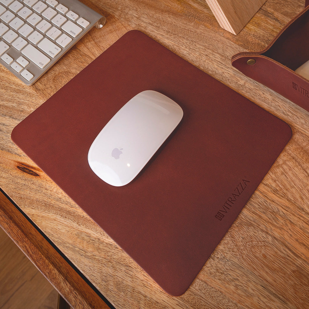 #color_mahogany alt="A white wireless mouse is placed on a brown leather mouse pad on a wooden desk. In the background, there is a silver keyboard and part of a wooden monitor stand. The mouse pad has the brand name "VITRAZZA" on it.
