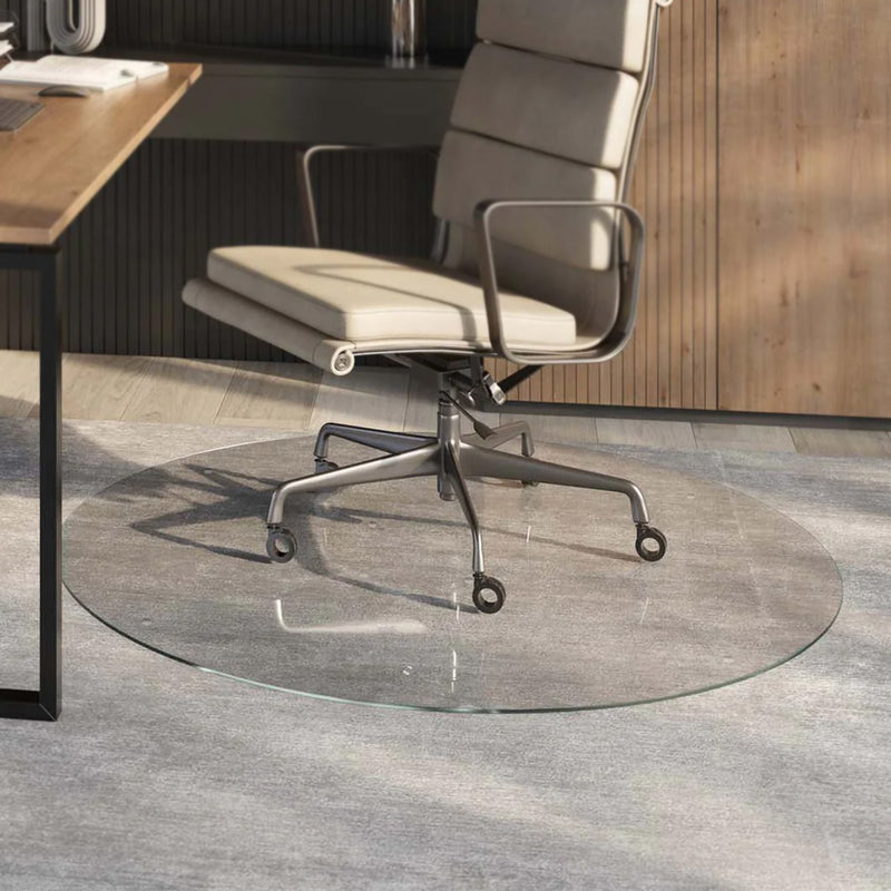 A modern office chair with a light-colored cushioned seat and backrest, mounted on a metal frame with casters, is positioned on a Round Glass Chair Mat. The chair is placed in front of a wooden desk in a contemporary office setting with wooden paneling in the background.