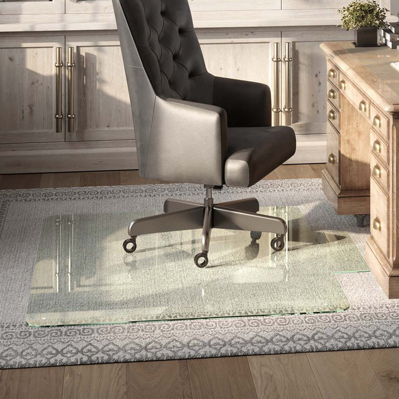 Black leather office chair on a Tabbed Glass Chair Mat over a patterned rug, in front of a classic wooden desk with brass handles, set against light wooden cabinetry.