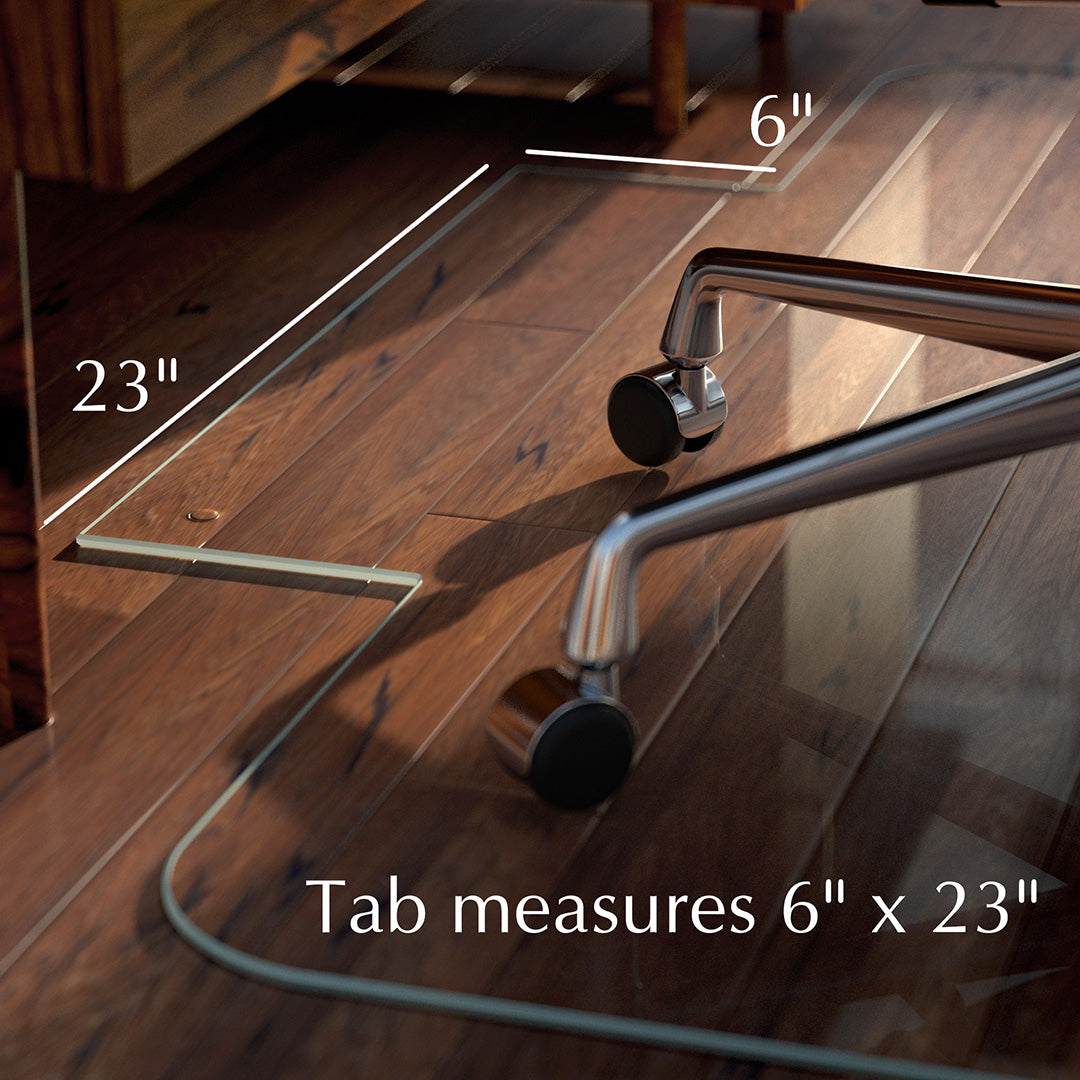 A close-up image of a glass chair mat on a wooden floor, showing a tab extension. The tab measures 6 inches by 23 inches, as indicated by the text and dimensions in the image. Part of an office chair with wheels is visible on the mat.
