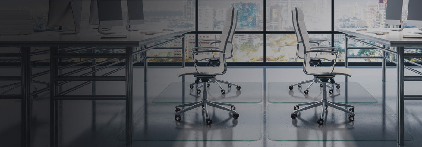 A modern office setting with two white ergonomic office chairs positioned in front of large windows showcasing a city skyline. The chairs are placed on glass chair mats, and there are desks with computer monitors in the background. The overall ambiance is sleek and professional, with a focus on a clean, organized workspace.