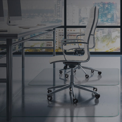 A modern office setting with two white ergonomic office chairs positioned in front of large windows showcasing a city skyline. The chairs are placed on clear glass chair mats, and there are desks with computer monitors in the background. The overall ambiance is sleek and professional, with a focus on a clean, organized workspace.