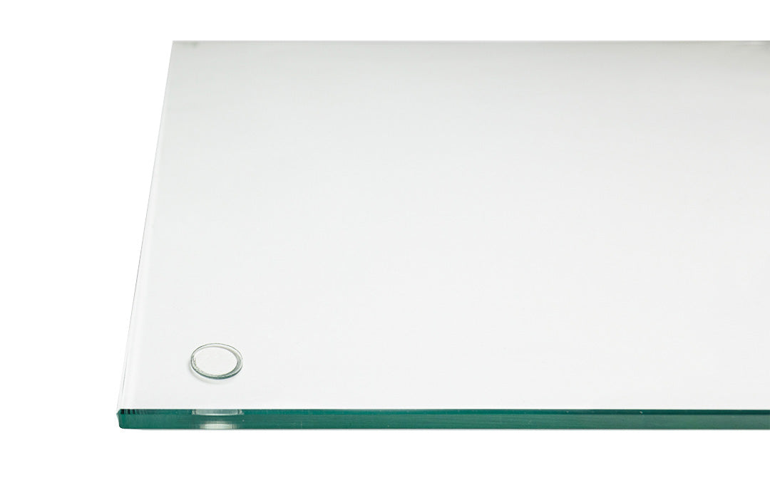 Close-up of a corner of a clear glass "DeskGuard" desk blotter, with a "Stabil-a-dot" visible near one edge. The glass edge is light in color with a subtle green undertone. The background is white, emphasizing the transparency of the glass.