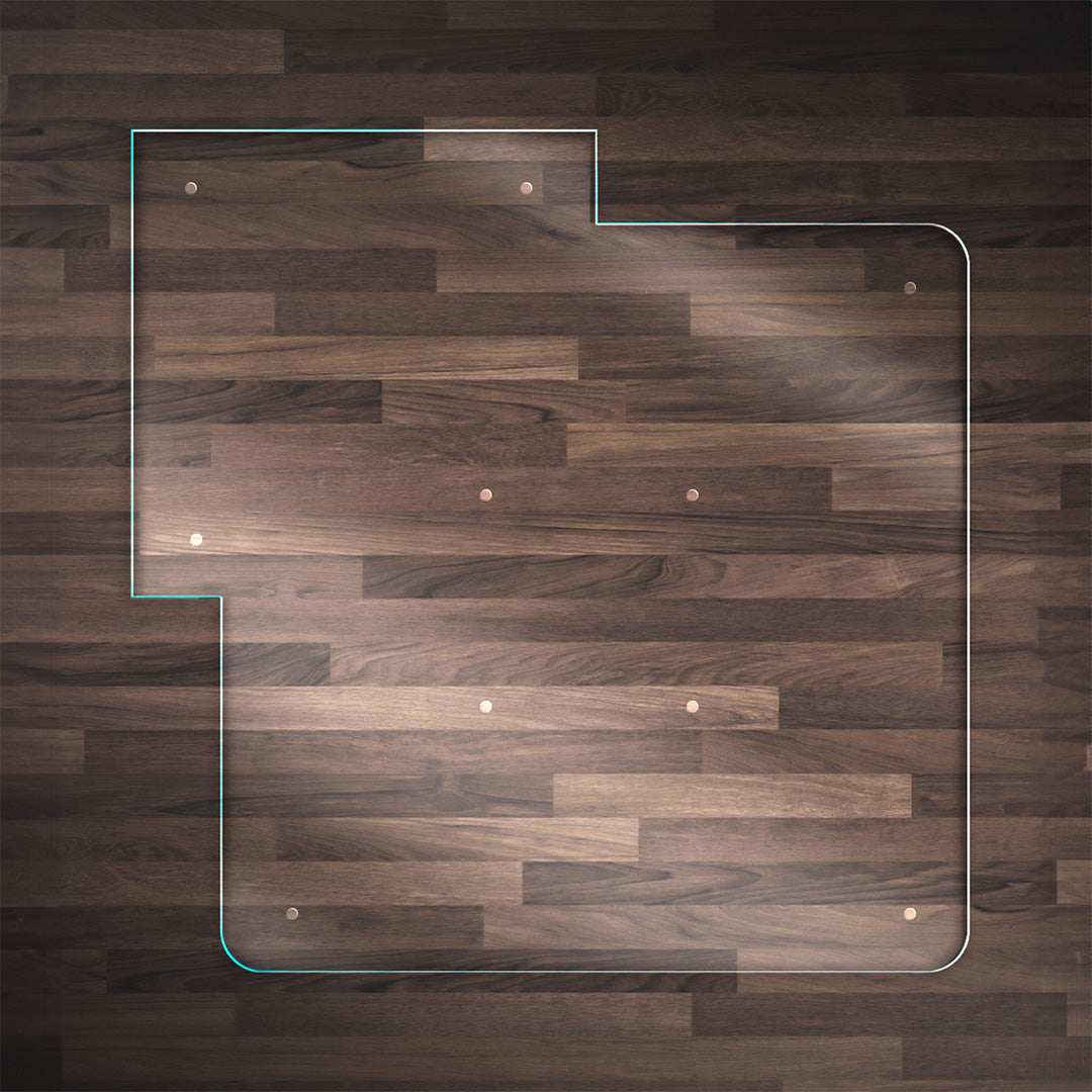 A clear glass chair mat with a "TAB" on the left side and top, placed on a dark wood floor, with rounded corners and "Stabil-a-dots" at each corner for grip. The wood floor has a rich, natural grain pattern.