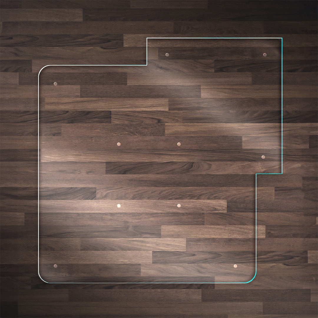 A clear glass chair mat with a "TAB" on the right side and top, placed on a dark wood floor, with rounded corners and "Stabil-a-dots" at each corner for grip. The wood floor has a rich, natural grain pattern.