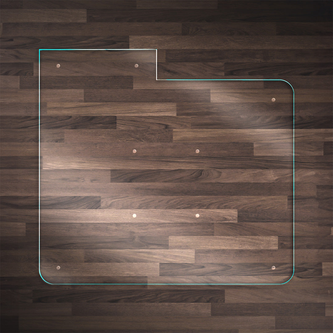 A clear glass chair mat with a "TAB" on the left side, placed on a dark wood floor, with rounded corners and "Stabil-a-dots" at each corner for grip. The wood floor has a rich, natural grain pattern.