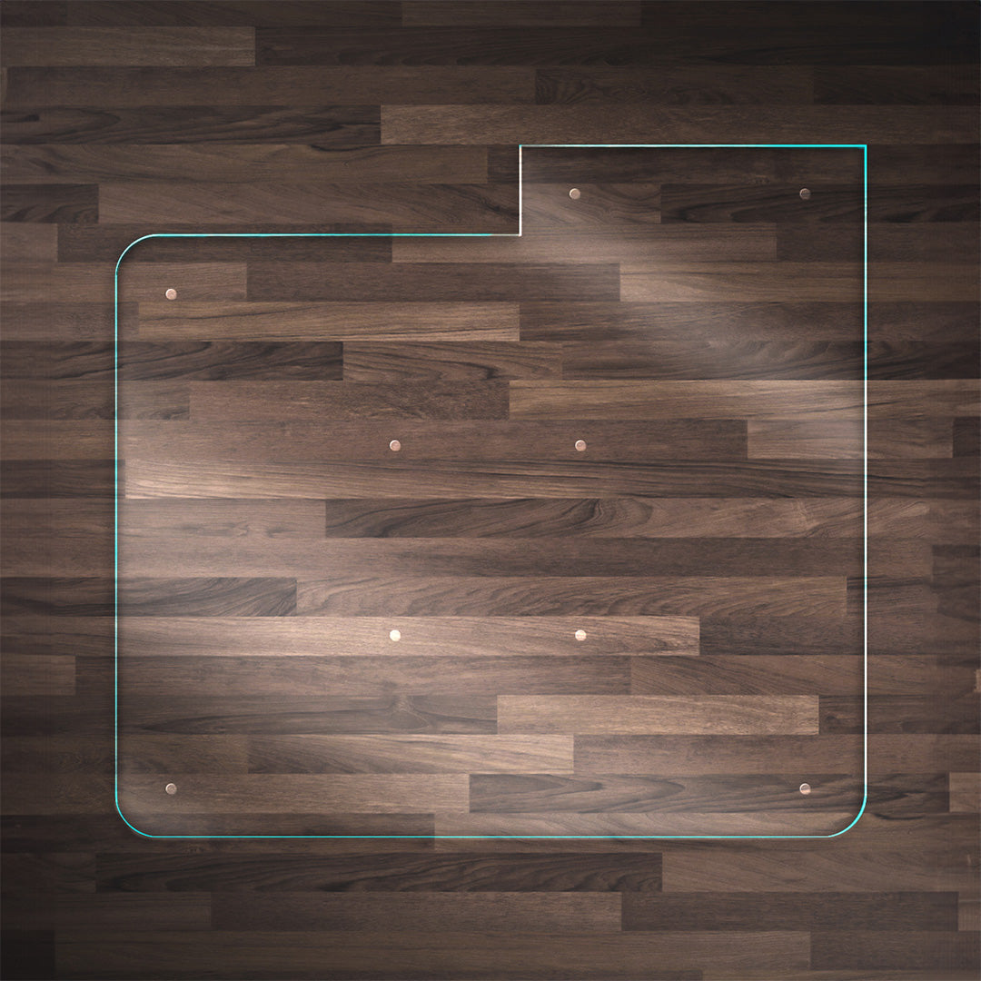 A clear glass chair mat with a "TAB" on the right side, placed on a dark wood floor, with rounded corners and "Stabil-a-dots" at each corner for grip. The wood floor has a rich, natural grain pattern.