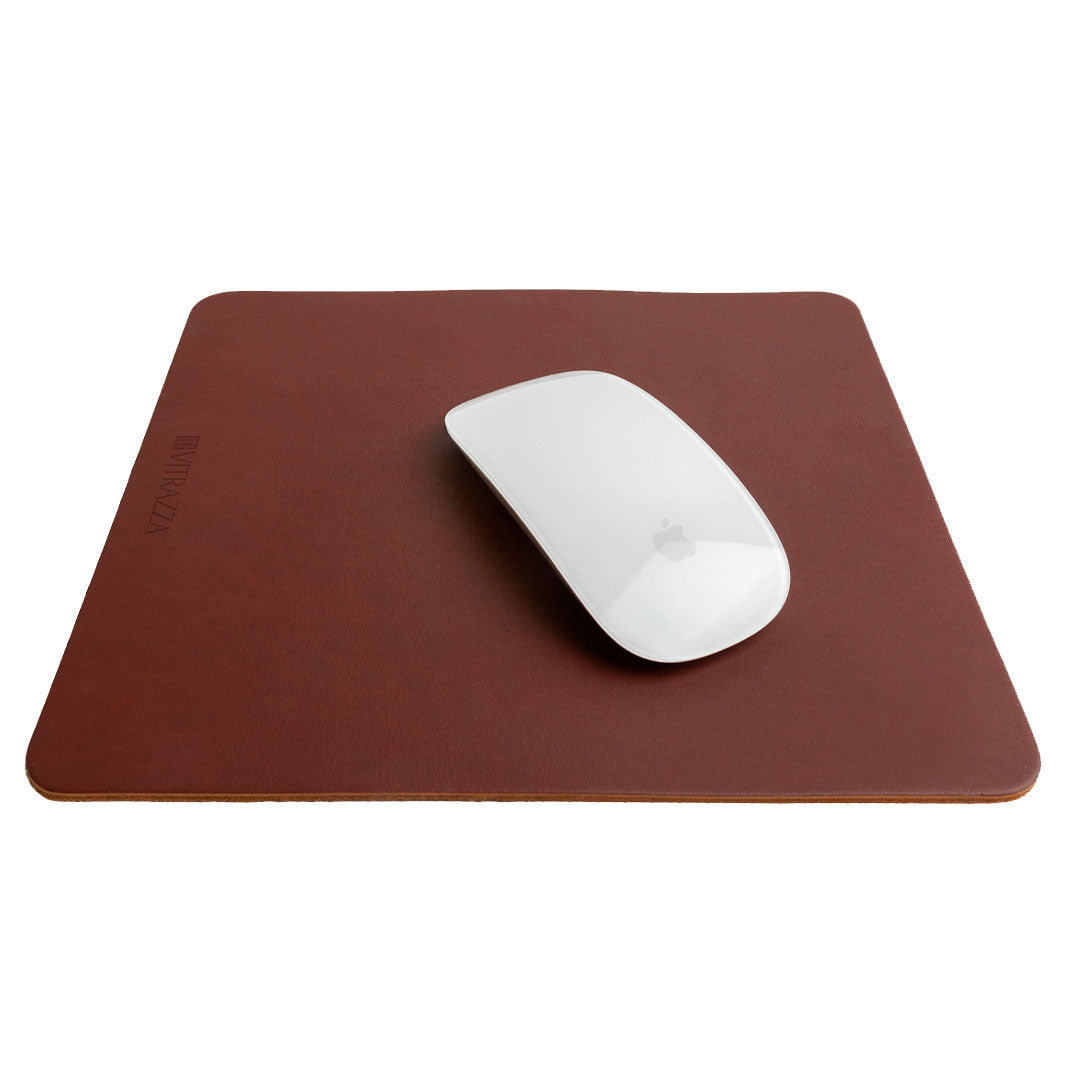 #color_mahogany a;t="A white wireless mouse is placed on top of a brown leather mouse pad. The mouse pad has the brand name "VITRAZZA" on it. The background is plain white."