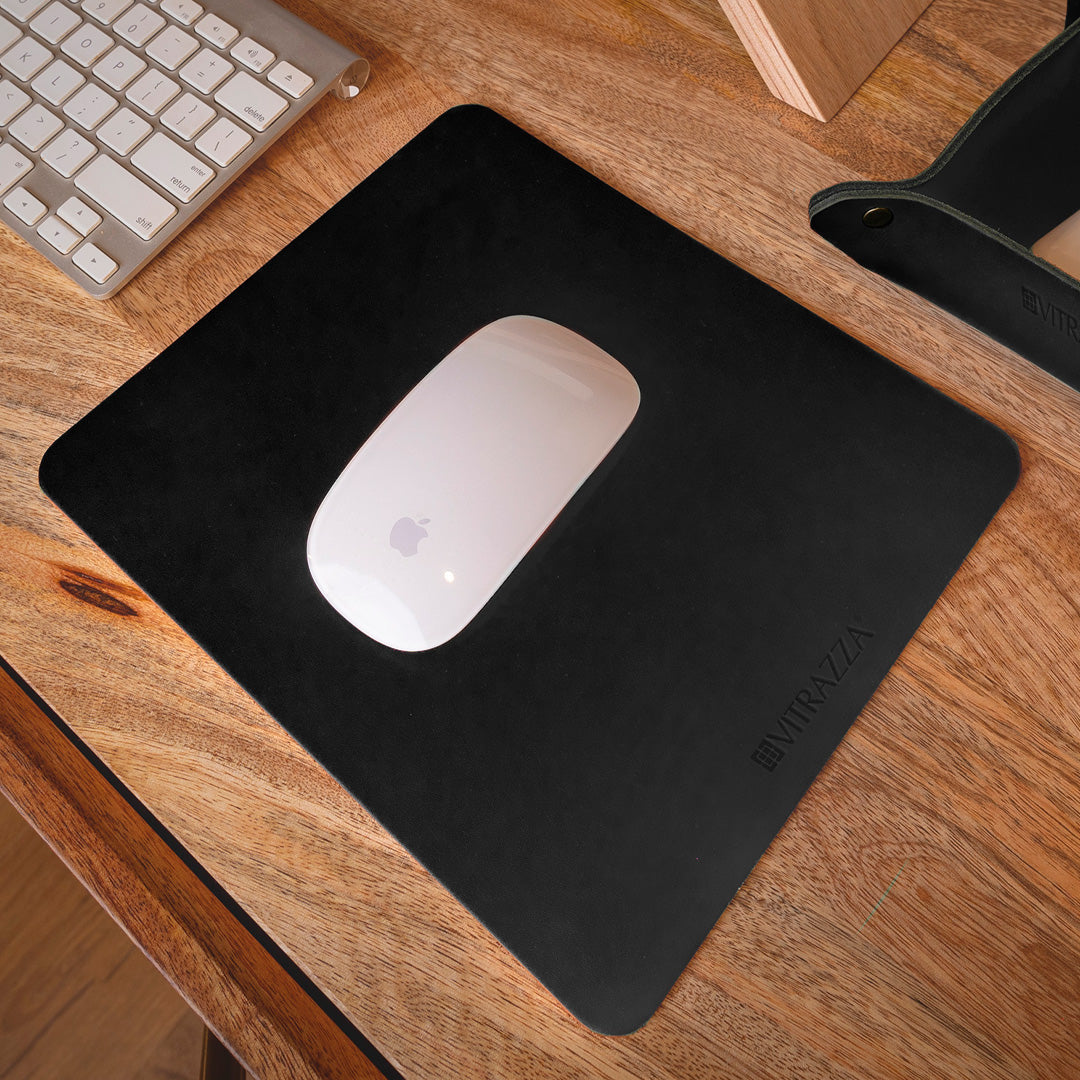 #color_charcoal alt="A white wireless mouse is placed on a black leather mouse pad on a wooden desk. In the background, there is a silver keyboard and part of a wooden monitor stand. The mouse pad has the brand name "VITRAZZA" on it.