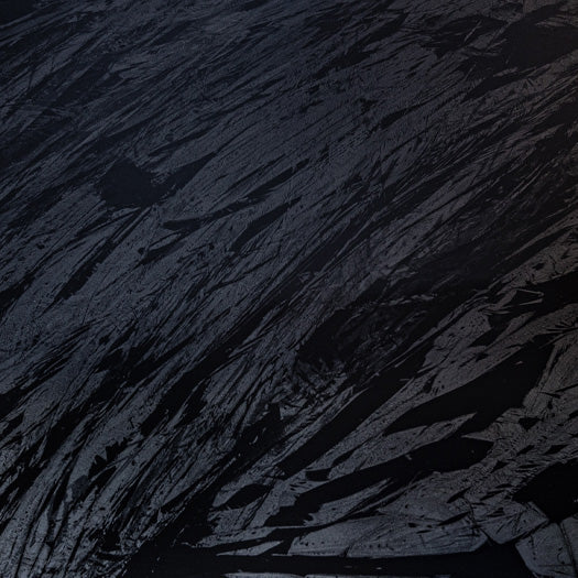 "A close-up view of a textured surface with a dark, abstract pattern resembling cracked earth or a rugged terrain, with shades of black and grey."