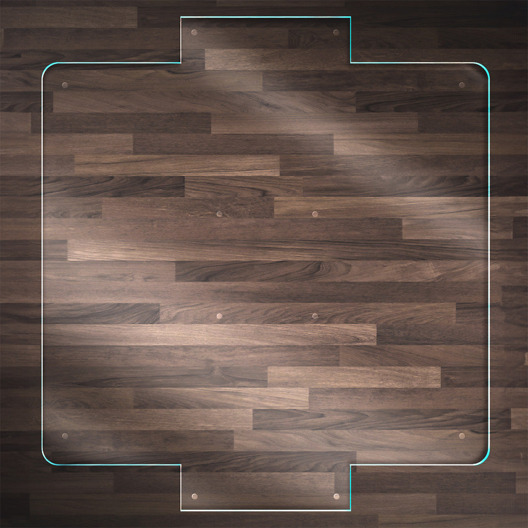A clear glass chair mat with a front and back facing "TAB",  placed on a dark wood floor, with rounded corners and "Stabil-a-dots" at each corner for grip. The wood floor has a rich, natural grain pattern.