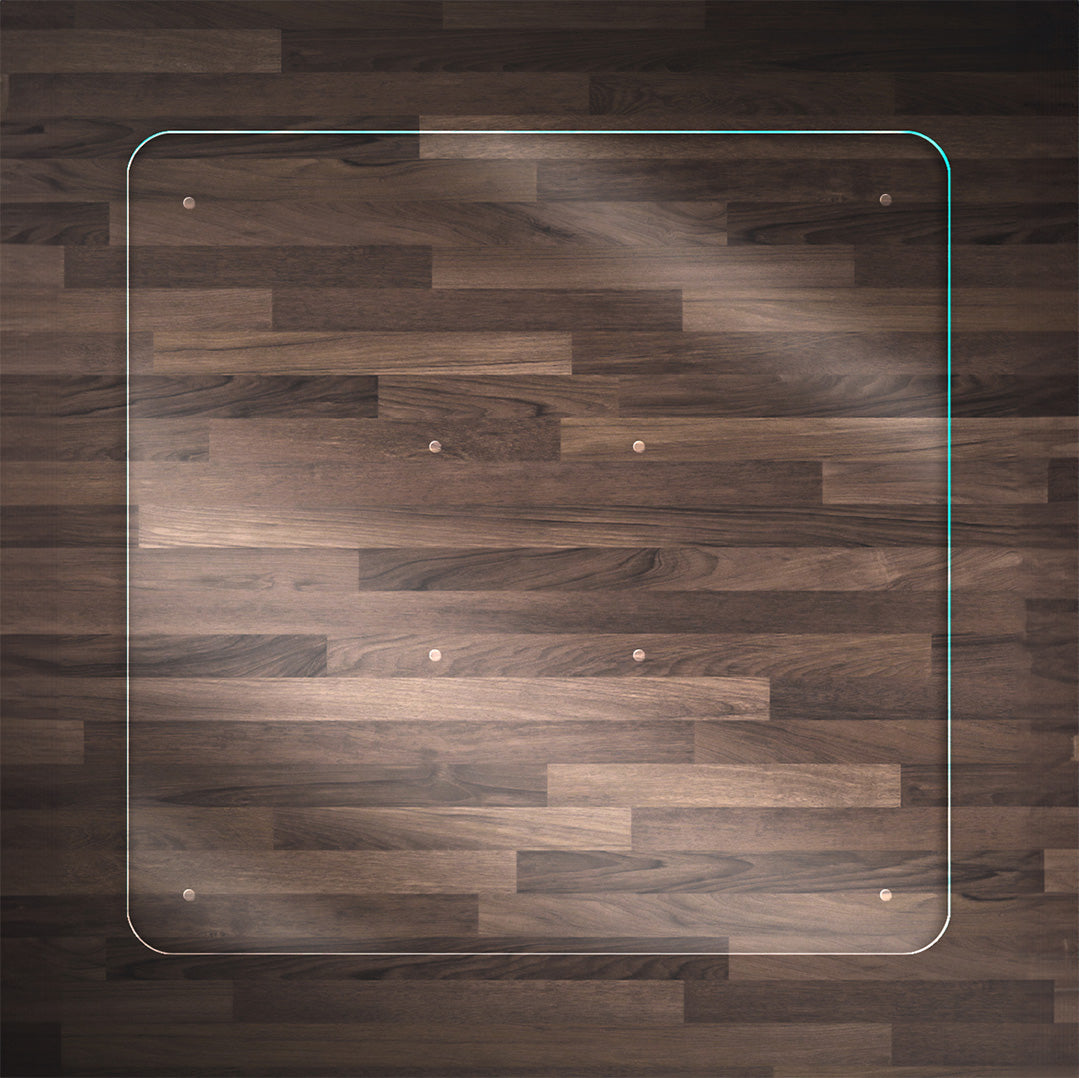 A clear Square or Rectangle glass chair mat placed on a dark wood floor, with rounded corners and "Stabil-a-dots" at each corner for grip. The wood floor has a rich, natural grain pattern.