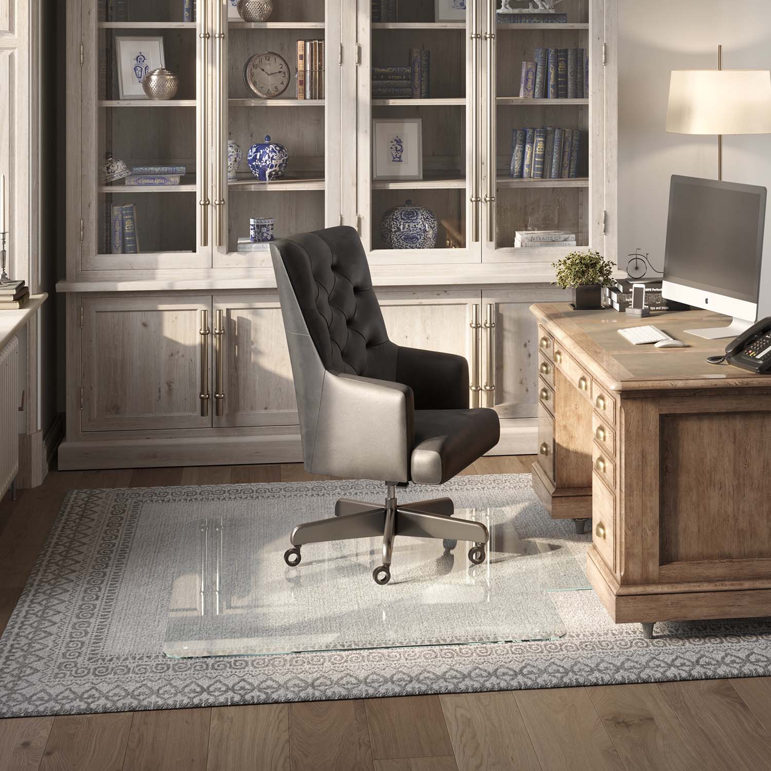 #glass clarity_luminoso (low-iron ultra clear) alt="A home office with a wooden desk, computer, and black leather chair on a 46" x 60" "luminoso" tab glass chair mat over a patterned rug. Behind is a cabinet with glass doors displaying books and decor."
