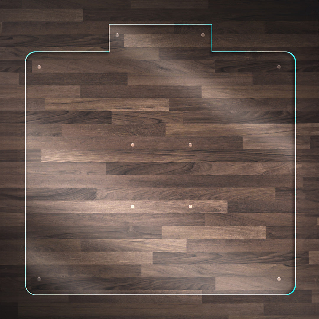 A clear glass chair mat with a "TAB" centered on the front side, placed on a dark wood floor, with rounded corners and "Stabil-a-dots" at each corner for grip. The wood floor has a rich, natural grain pattern.